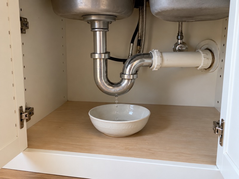 A small kitchen sink leak with water caught in a bowl